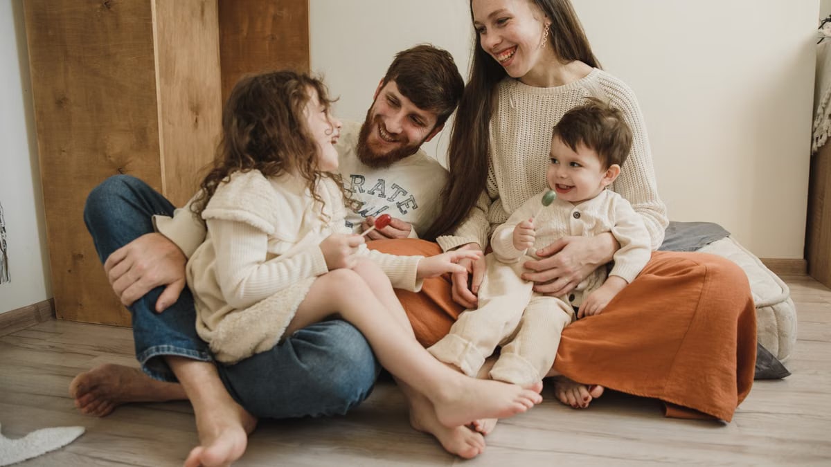 Smiling family of four sitting on the living room floor, enjoying quality time together.